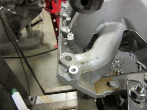 Close-up of an engine intake manifold being worked on with a drill press