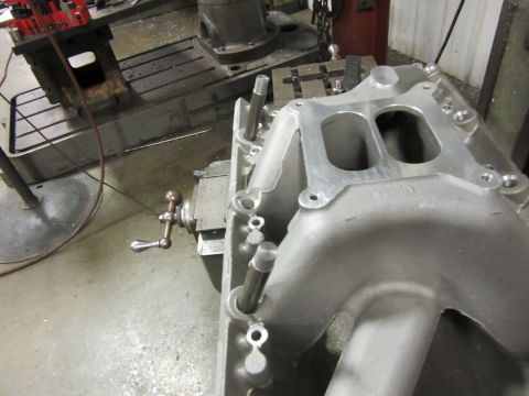 Aluminum intake manifold with dual openings, on a workbench with machinery