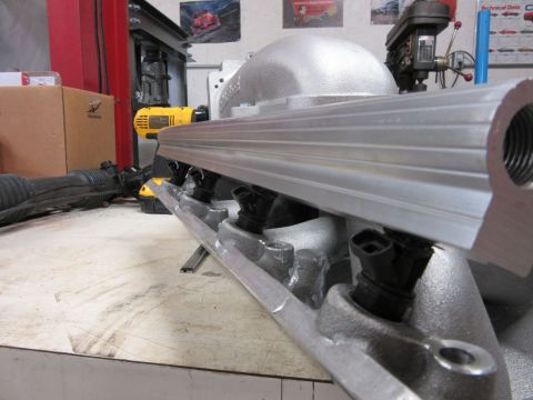 Close-up of an aluminum fuel rail with injectors attached, resting on a workbench