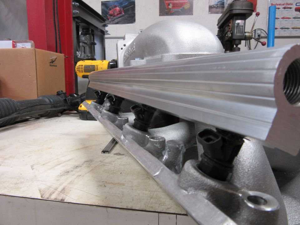 Close-up of an aluminum fuel rail with injectors attached, resting on a workbench