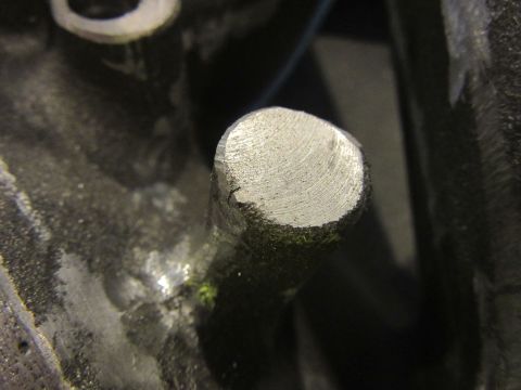 Close-up of a metal pin protruding from a dark, textured surface, possibly an engine block