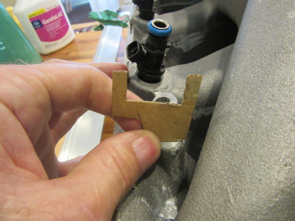 hand holding cardboard template near fuel injector on intake manifold