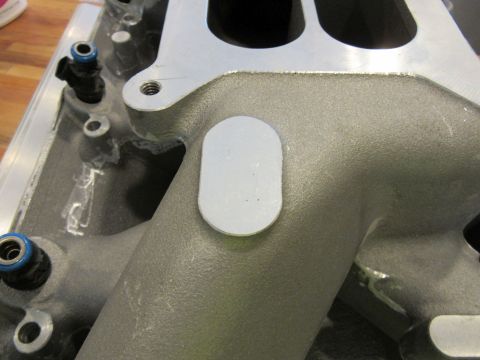 Close-up of an engine intake manifold with fuel injectors and a white oval sticker