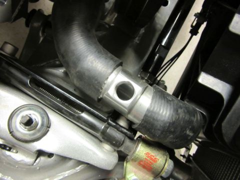 Close-up of a black rubber hose connected to a metal fitting with a hole, part of an engine