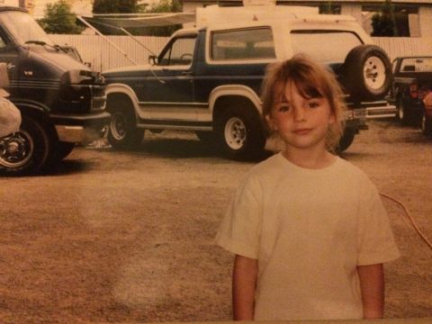 1989 Ford Bronco - A young girl stands in front of a dark blue and white Ford Bronco.
