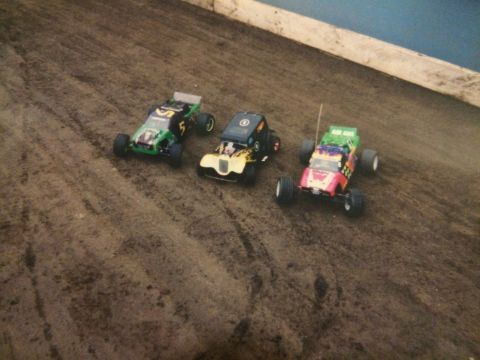 1989 Ford Bronco - Three remote control race cars, one green and black, one yellow and black, and one pink and green, line up on a dirt track.