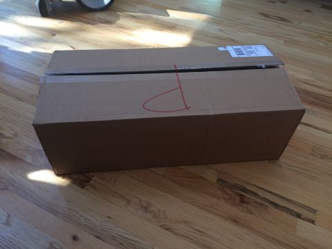 1989 Ford Bronco - A cardboard box with a red marking sits on a wooden floor, with a shipping label on top.