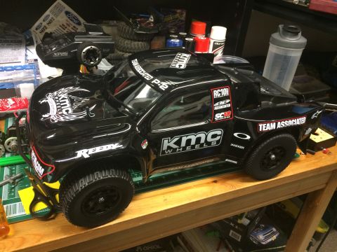 1989 Ford Bronco - A remote-controlled truck with various sponsor decals is displayed on a wooden surface, surrounded by hobby supplies.