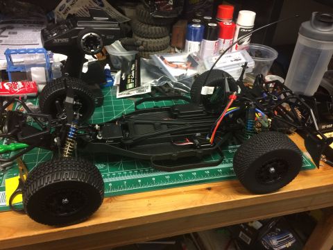 1989 Ford Bronco - A disassembled remote control car chassis sits on a workbench, surrounded by hobby supplies and tools.