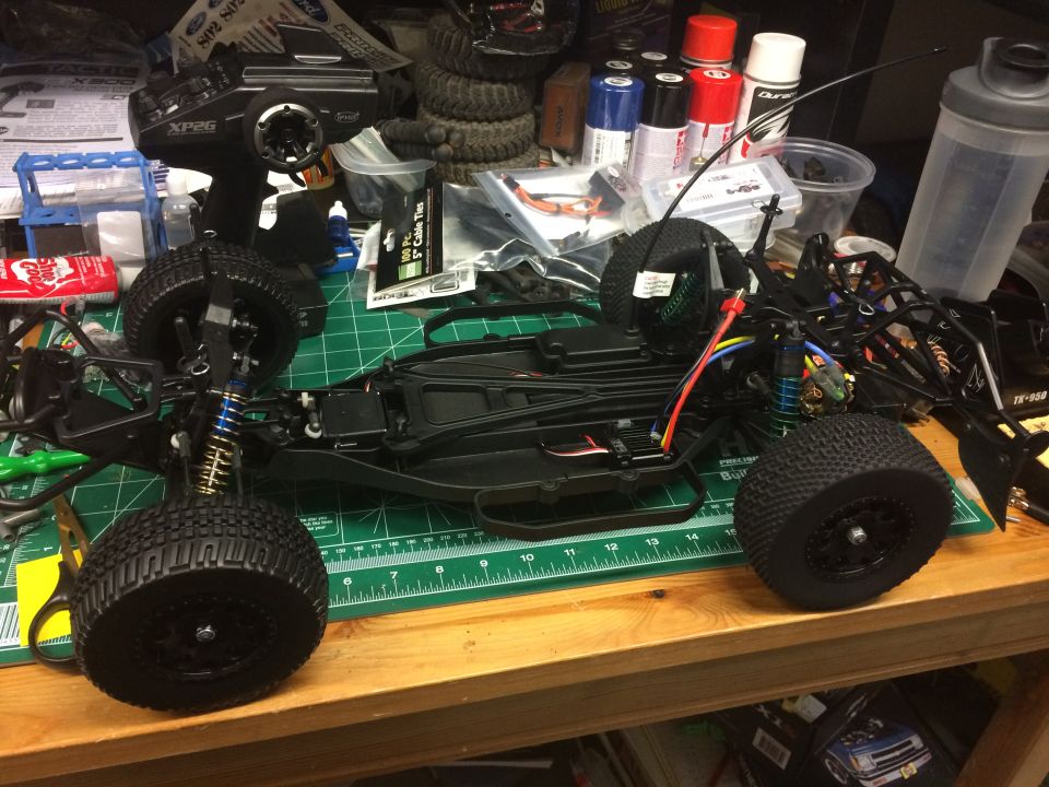 Black remote control car chassis with blue shocks and knobby tires on a green cutting mat