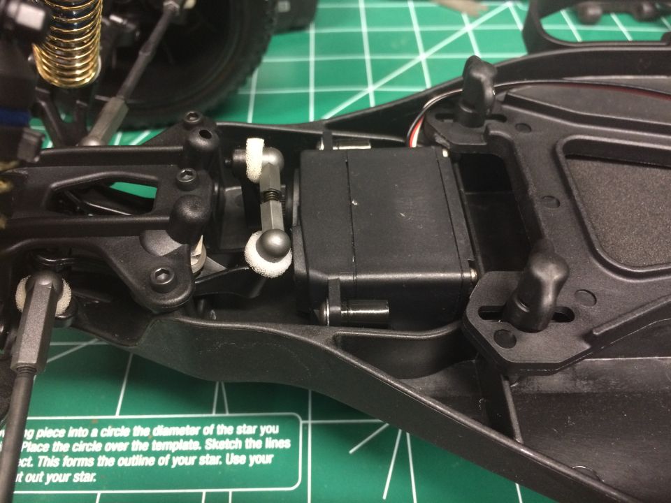 RC car chassis showing servo motor and suspension components on a cutting mat