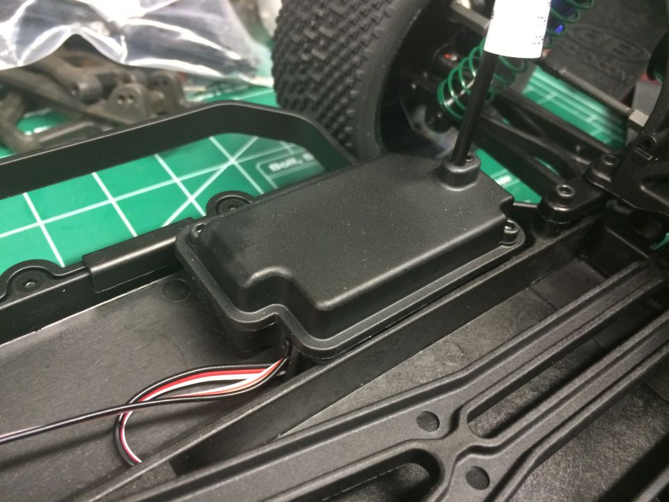 Remote control car chassis with black plastic frame, green shock absorber, and wiring. Close-up view