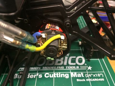 1989 Ford Bronco - Close-up of an electric motor for an RC car, showing wiring connections on a hobby cutting mat.