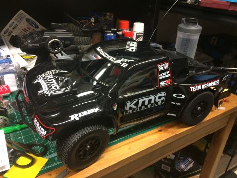 1989 Ford Bronco - A black remote-controlled truck with various sponsor decals sits on a wooden workbench, surrounded by tools and parts.