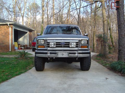 1986 Ford Bronco - Front view of a dark gray/silver 1980s Ford Bronco SUV with a chrome grille bearing the Ford name, brushguard, chrome bumper, and large mud…