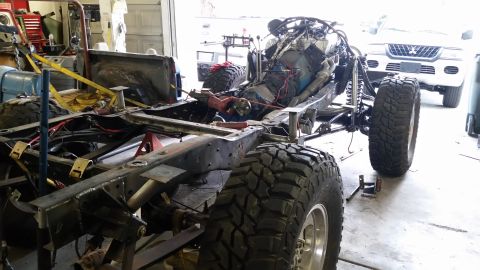 1979 Ford Bronco - A heavily modified vehicle chassis is shown in a garage setting, with a white SUV visible in the background. The chassis appears to be unde…