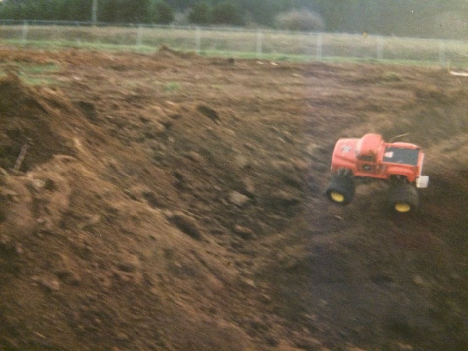 Orange remote-controlled monster truck with large tires on a dirt hill.