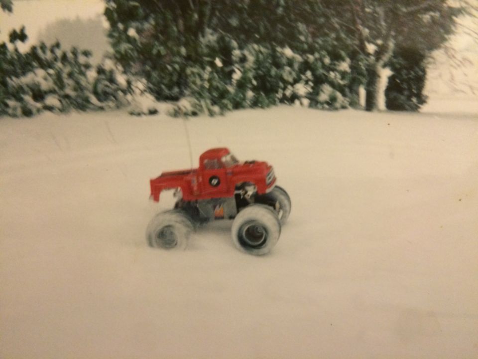 Red remote-controlled monster truck driving in the snow