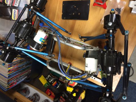 1989 Ford Bronco - A close-up overhead view of the chassis and drivetrain of a custom-built RC car, featuring blue aluminum suspension components and black ge…