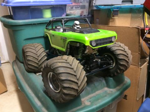 1989 Ford Bronco - A bright green RC monster truck, resembling a Ford Bronco, sits on top of a green plastic storage bin. The truck features oversized tires a…
