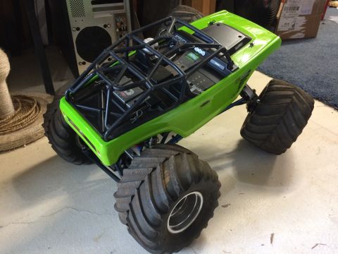 1989 Ford Bronco - A bright green remote-controlled monster truck with a black roll cage sits on a concrete floor, angled towards the viewer's right. It featu…