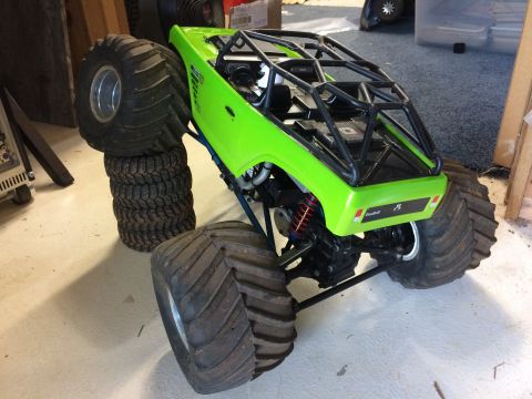 1989 Ford Bronco - A bright green remote-controlled monster truck with oversized tires is shown in a garage setting. The truck features a roll cage and visibl…