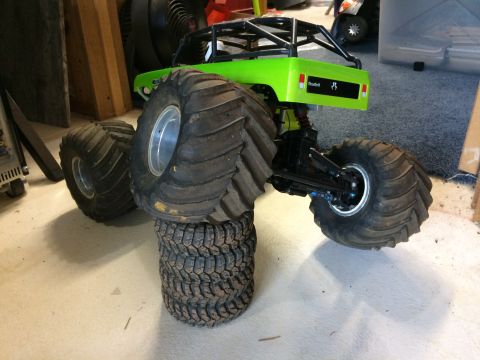 1989 Ford Bronco - A bright green RC monster truck with oversized tires is shown from a rear-side angle. The truck is elevated by a stack of tires, showcasing…
