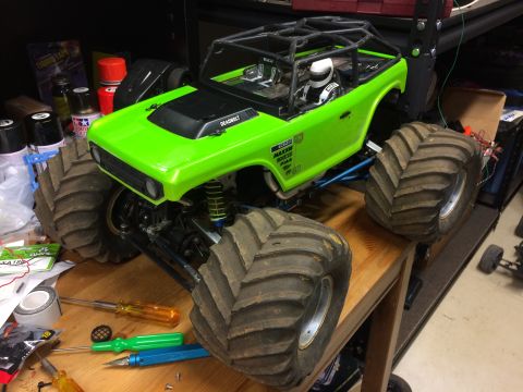 1989 Ford Bronco - A bright green remote-controlled monster truck with large, knobby tires sits on a wooden workbench. Tools and various hobby supplies are sc…