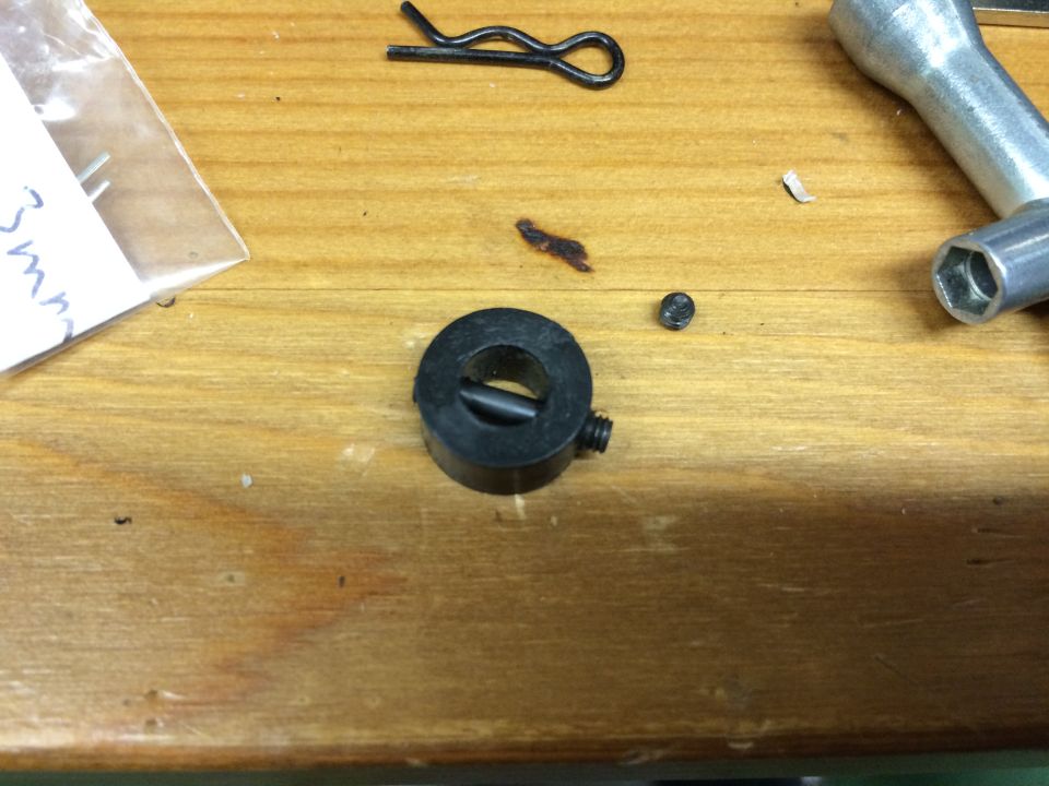 Small metal parts including a black collar, set screw, and hairpin clip on a wooden surface.
