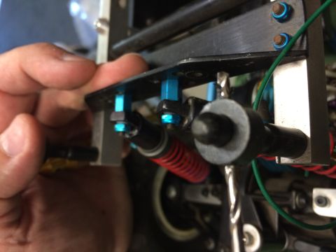 1989 Ford Bronco - A hand is shown holding a blue aluminum shock mount bracket with a black shock absorber attached to a vehicle's chassis. The shock absorber…