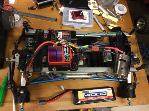 1989 Ford Bronco - A remote-controlled car chassis is shown on a wooden table, with various electronic components and tools scattered around. The chassis feat…
