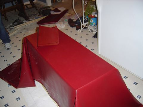 1986 Ford Bronco - Maroon vinyl upholstery material draped over a long rectangular object on a checkered kitchen floor during a DIY interior re-covering proje…