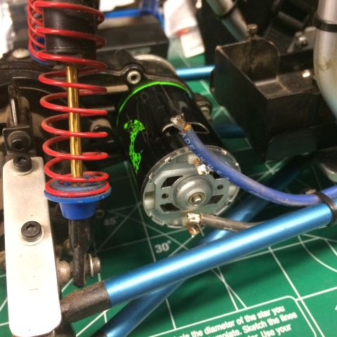 1989 Ford Bronco - A close-up view shows the electric motor and suspension components of a remote-controlled vehicle, likely an RC car, resting on a green cut…