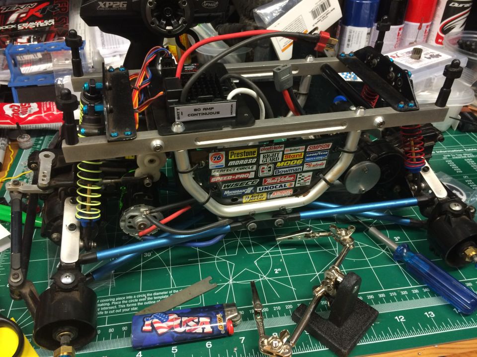 Remote control car chassis with electronics, suspension, and decals on a green cutting mat.