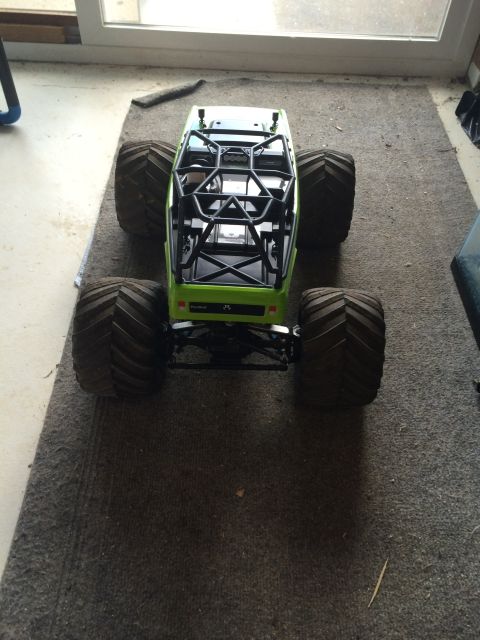 1989 Ford Bronco - A bright green remote-controlled monster truck with large, knobby tires sits on a gray carpet. The vehicle has a black roll cage over the o…