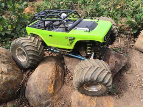 1989 Ford Bronco - A bright green RC rock crawler with oversized tires is navigating a rocky terrain. The vehicle features a black roll cage and detailed inte…
