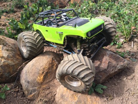 1989 Ford Bronco - A bright green remote-controlled rock crawler with large, knobby tires is navigating over large rocks and dirt.