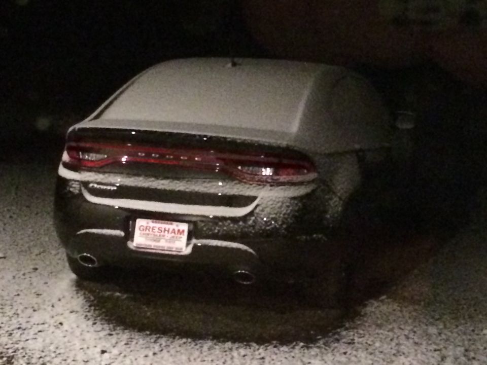 Rear view of a snow-covered dark Dodge Dart at night with a Gresham Chrysler Jeep license plate frame.