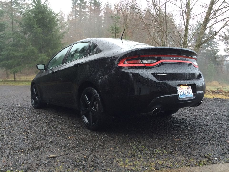 Black 2015 Dodge Dart, rear driver's side view, parked on gravel in the rain.