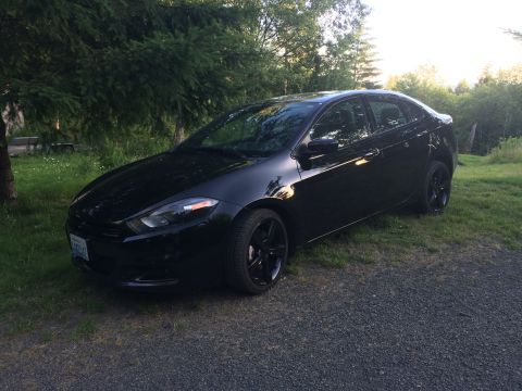 2015 Dodge Dart - A black Dodge Dart sedan is parked on a gravel driveway next to a grassy area with trees in the background. The car is angled towards the v…