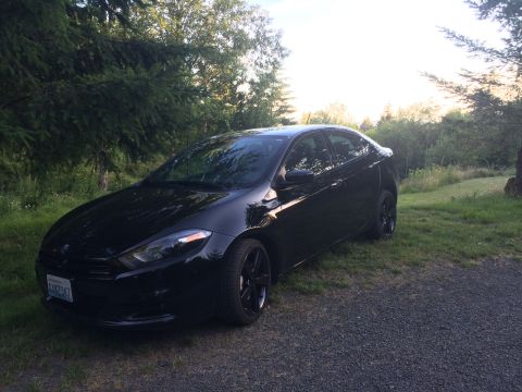 2015 Dodge Dart - A black 2015 Dodge Dart sedan is parked on a gravel driveway next to a grassy area with trees in the background.