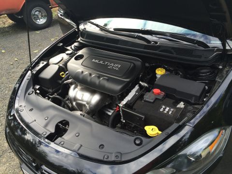 2015 Dodge Dart - The engine bay of a black Dodge Dart is shown with the hood open. The MULTIAIR 2.4L engine cover, battery, and various fluid reservoirs are…