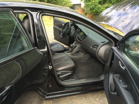 2015 Dodge Dart - The interior of a black Dodge Dart is shown with the driver's side doors open. The dashboard, steering wheel, and front seats with red stit…