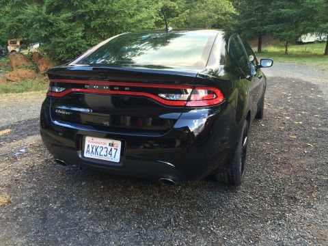 2015 Dodge Dart - The rear driver's side quarter view of a black 2015 Dodge Dart sedan is shown parked on a gravel driveway. The car has a Washington license…