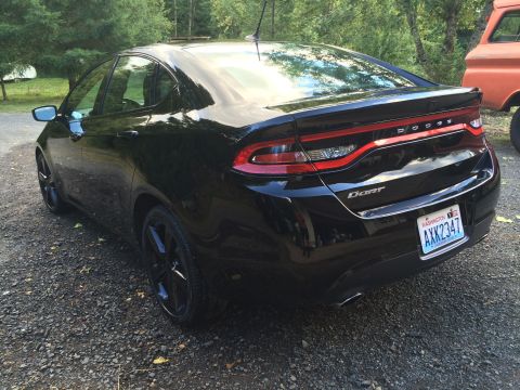 2015 Dodge Dart - The rear passenger side of a shiny black 2015 Dodge Dart sedan is shown parked on a gravel driveway. The car has black rims and a Washingto…