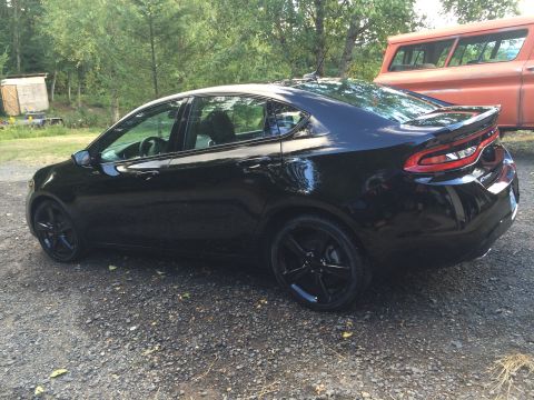 2015 Dodge Dart - A black 2015 Dodge Dart is parked on a gravel driveway next to a wooded area. The car is viewed from the rear three-quarter angle, showing…