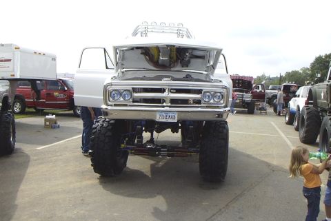 1995 Ford Bronco - A lifted white truck is parked at an outdoor event with its hood open, showing the engine compartment.