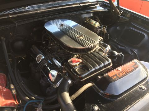 1962 Chevrolet Suburban - Close-up view of a black engine bay, featuring a chrome air cleaner assembly over a black engine with chrome valve covers. An orange and bl…