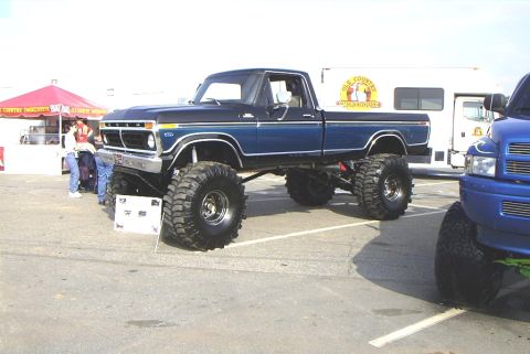 1995 Ford Bronco - This lifted pickup truck features a two-tone blue and black paint scheme with prominent off-road tires.