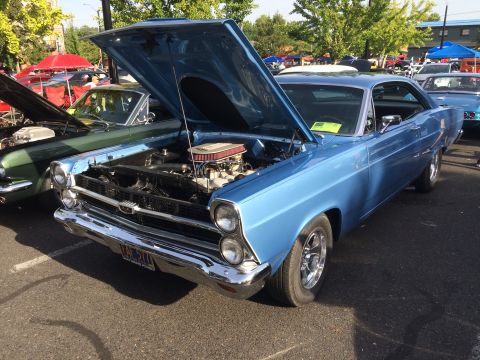 1962 Chevrolet Suburban - A light blue 1966 Ford Fairlane 500 is parked outside with its hood open, revealing the engine. Another classic car, a dark green coupe, is…